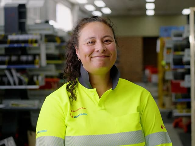 An Australia Post StarTrack team member smiles inside a parcel sorting depot.