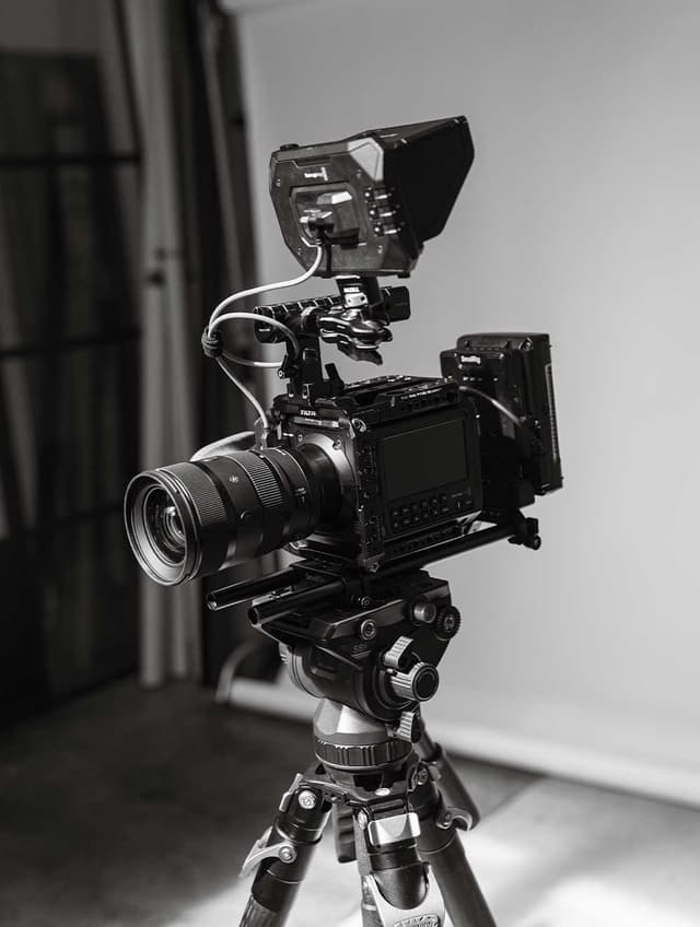 A professional cinema camera rig with a monitor and lens mounted on a tripod in a photography studio.