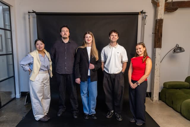 Five colleagues stand for a group portrait against a black backdrop in a studio.