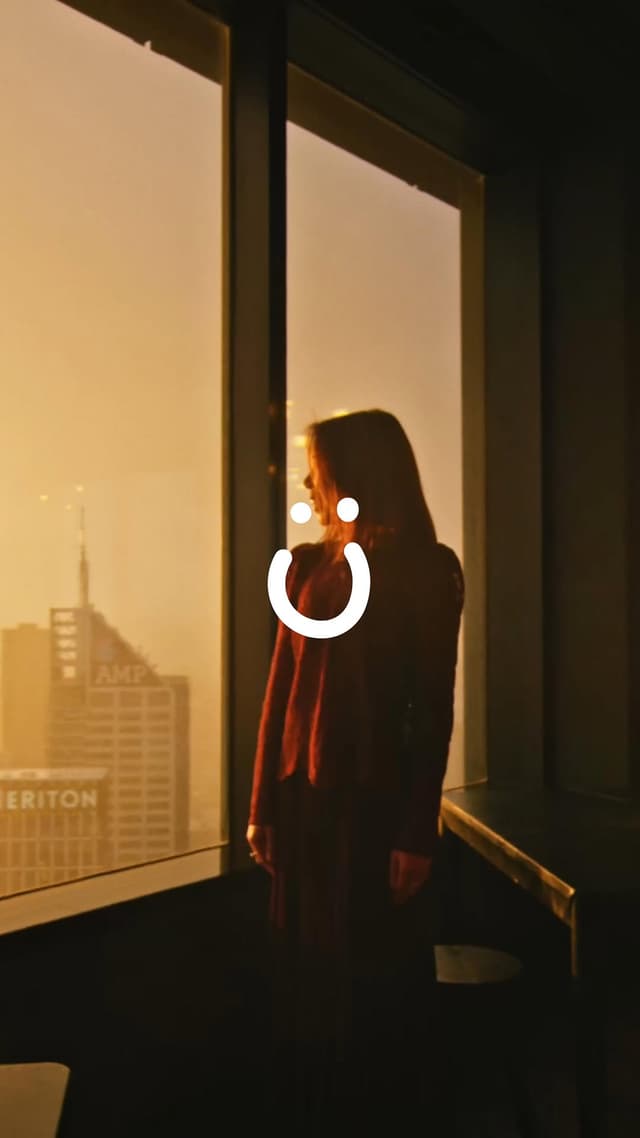 A woman looks out over the Melbourne skyline at sunset, with the Lucky Boy Agency smile logo overlaid.
