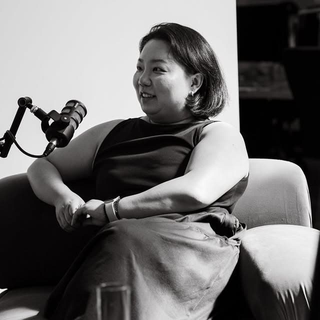 A black and white portrait shows a smiling woman seated with a microphone during a podcast recording.