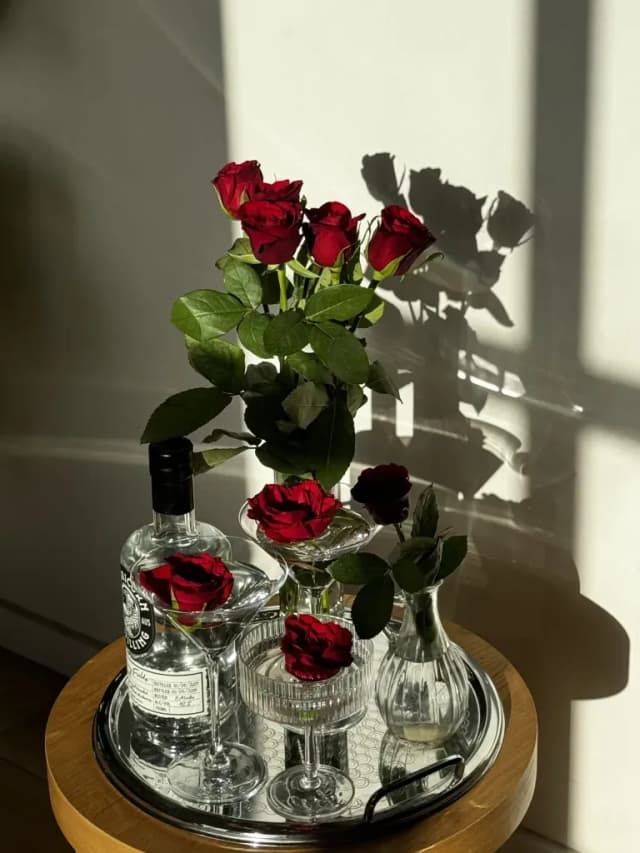 A Capricorn Distilling Co gin bottle sits among red roses and martini glasses on a silver tray.