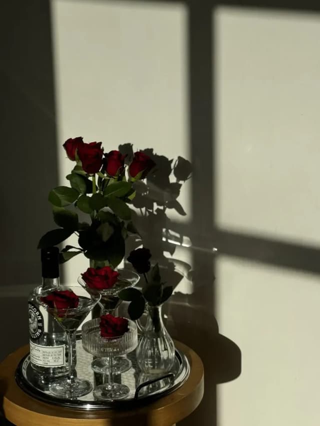 Red roses, martini glasses, and a bottle of Capricorn Distilling Co gin sit on a tray in warm window light.