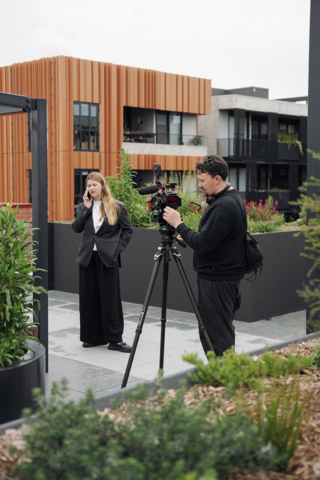 A woman talks on the phone while a camera operator films her on a rooftop terrace.