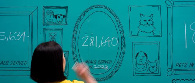 A woman draws on a teal wall mural showing pet portraits and the stat 281,640 meals served in 2023.
