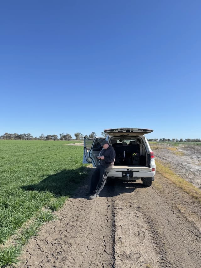 A man leans against a ute parked beside a green crop on a Providore Global farm.