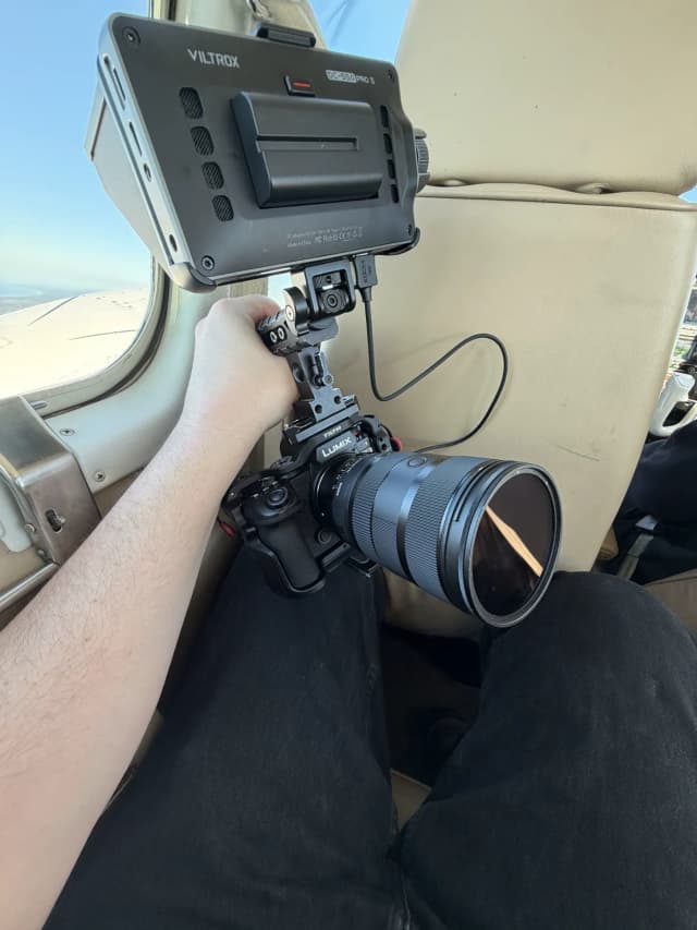 A hand holds a camera rig with a monitor inside a small plane during a Providore Global aerial shoot.