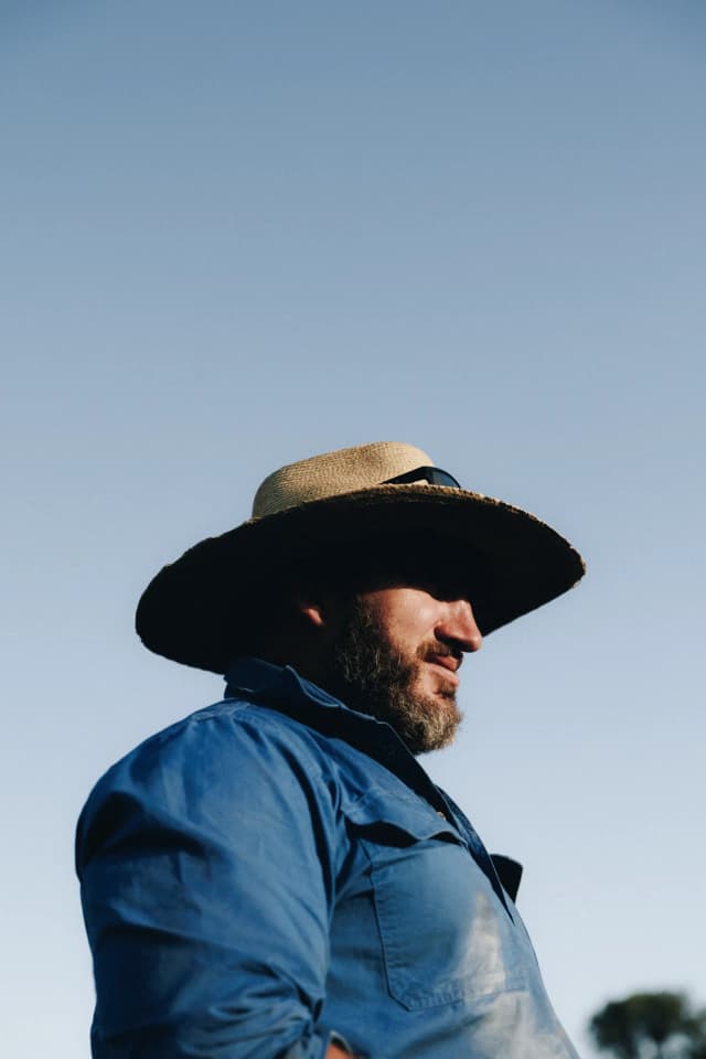 A grazier in a wide-brimmed hat and blue shirt looks out across a Providore Global property.
