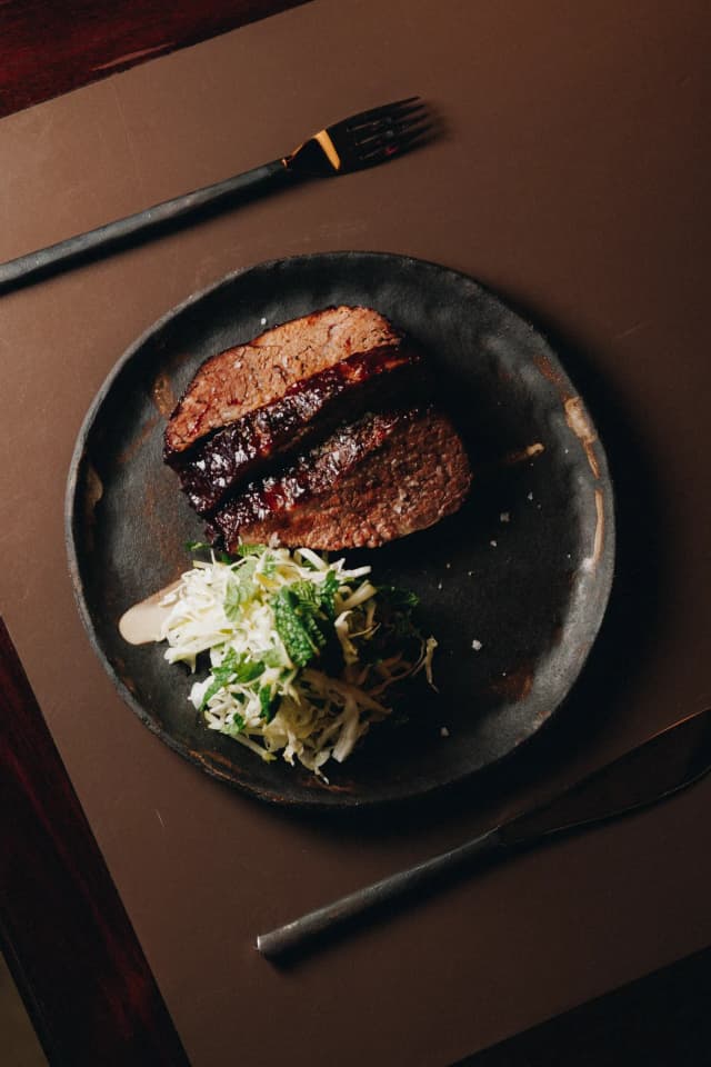 For Providore Global, a glazed sliced meat dish is plated with cabbage and mint slaw on a dark ceramic plate.