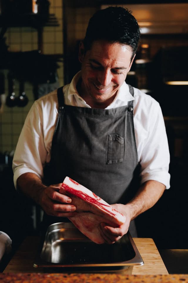 Chef Ian Oakes holding a beef rib over a tray in the kitchen at Mullumbimby