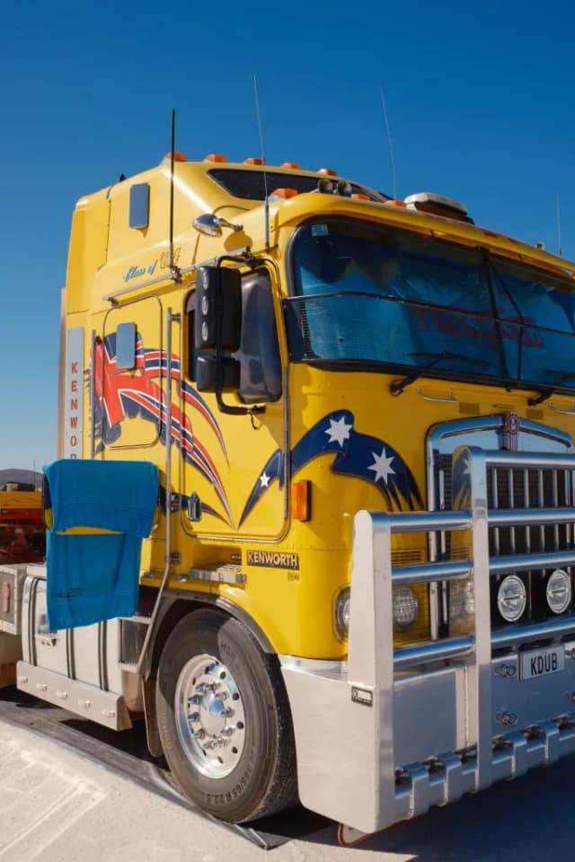 A yellow Kenworth truck decorated with Australian and British flag decals is parked under a clear blue sky.