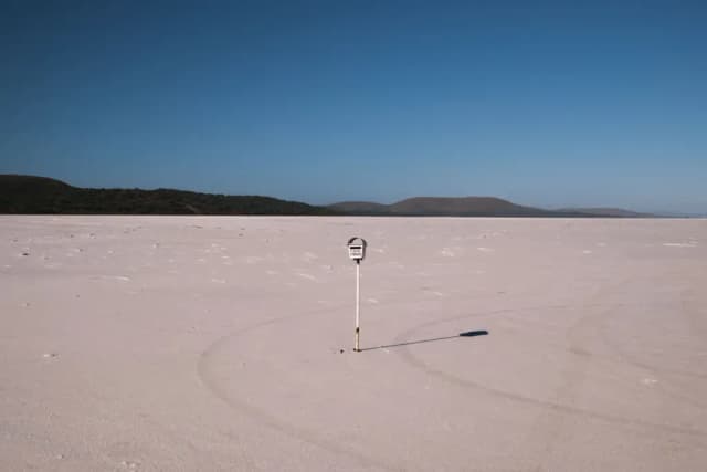 A lone marker post stands on a vast dry salt lake bed with curving tyre tracks in the foreground.