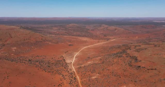 An aerial view of a dirt road winding through the red outback landscape near the salt lakes.