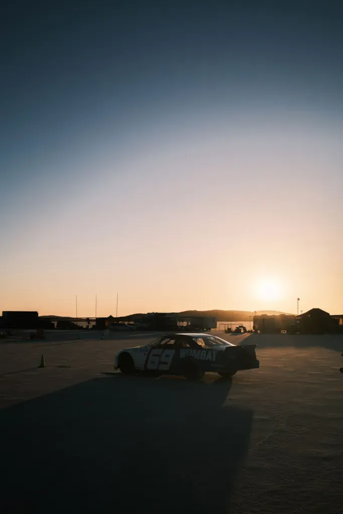 A vintage number 69 race car marked 'Wombat' sits parked on a salt flat at sunset.