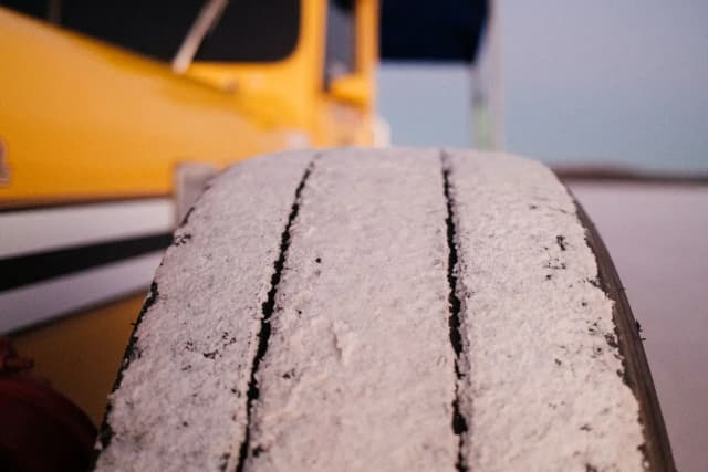A close-up of a truck tyre caked in white salt dust beside a yellow trailer at dusk.