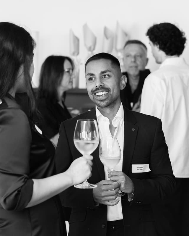 Black and white event photography of guests toasting wine glasses at a networking function.
