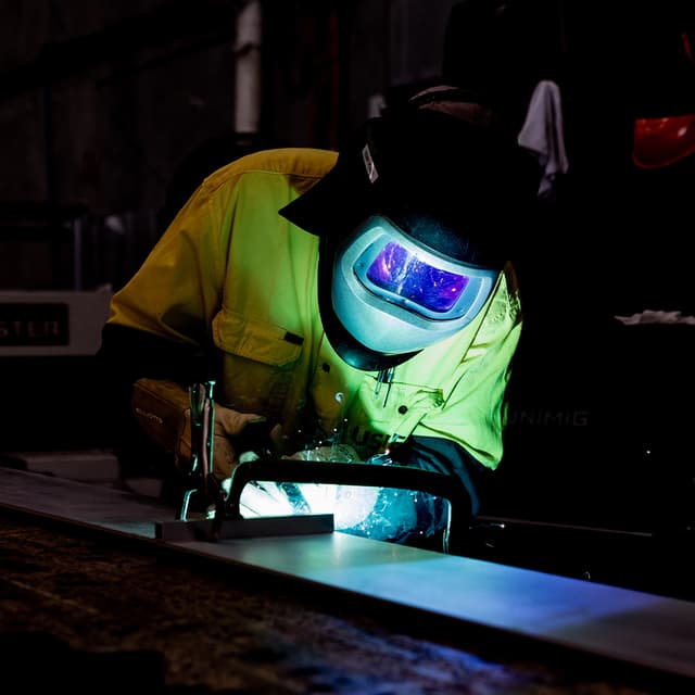 An Usher Group welder in a yellow hi-vis jacket and welding mask sends sparks flying while joining steel beams.