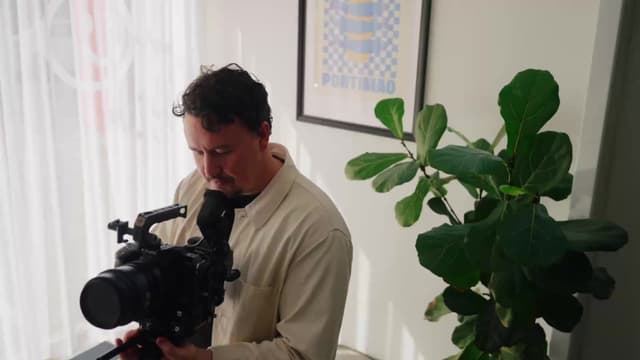 A videographer looks through a cinema camera viewfinder in a bright studio with a fiddle leaf plant.
