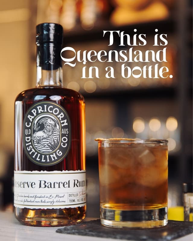 A bottle of Capricorn Distilling Co reserve barrel rum stands beside a poured cocktail with the tagline 'This is Queensland in a bottle.'