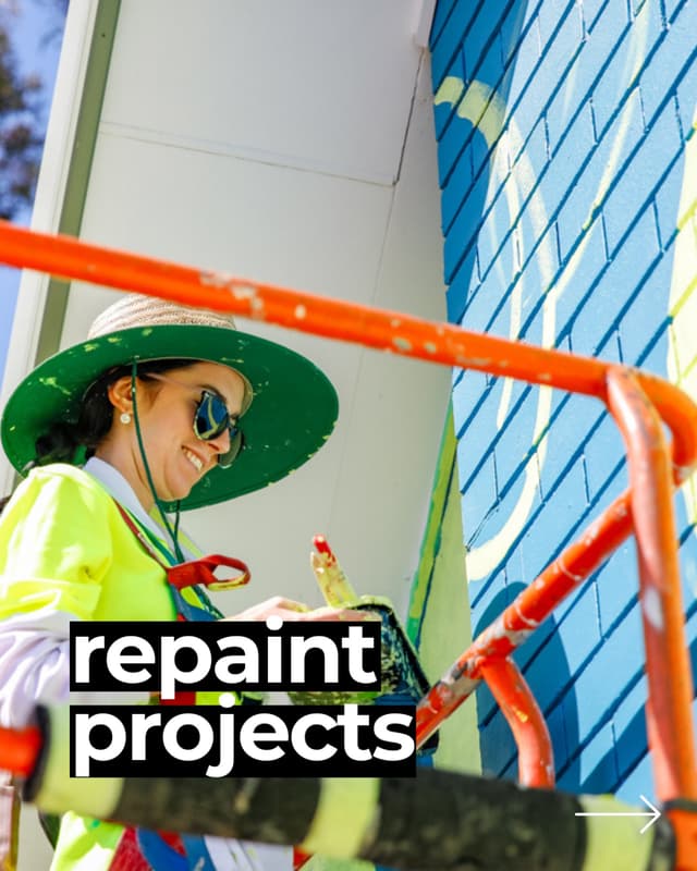 A painter in a wide-brimmed hat smiles while repainting a blue mural wall, captioned repaint projects.