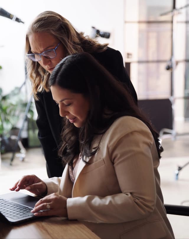 Two women review footage on a laptop together in a bright photography studio.