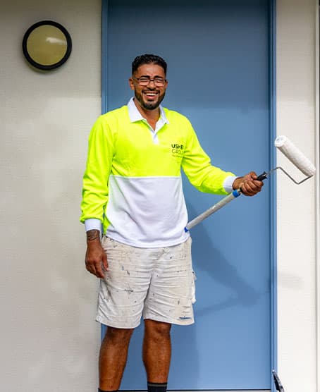 A tradesman in Usher Group hi-vis rolls paint onto a blue door outside a house.