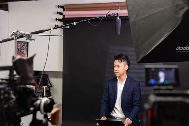 A man holds a cinema camera with a large lens in a bright indoor studio.