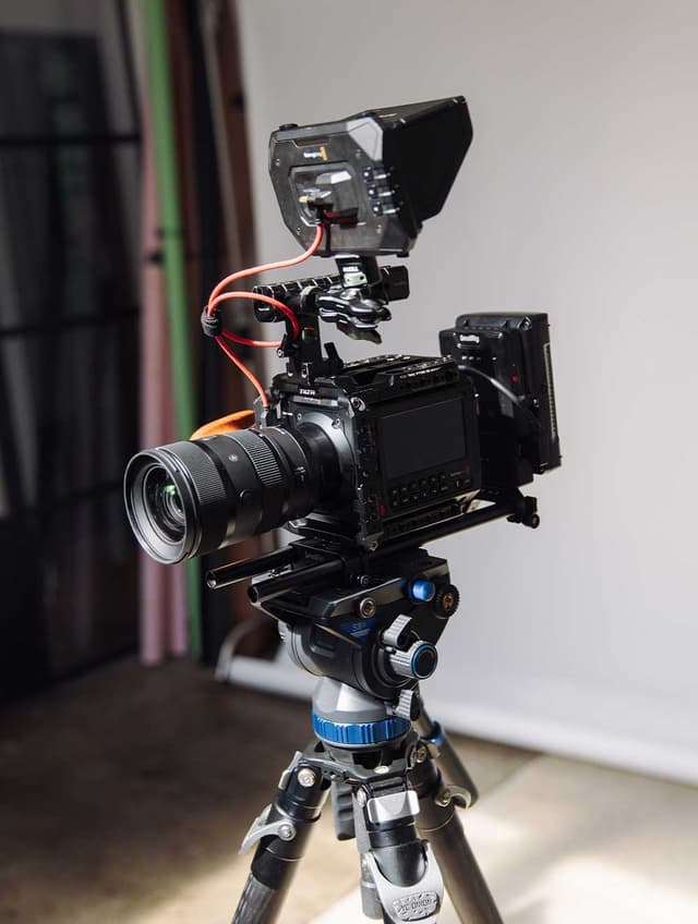 A cinema camera rig with a monitor and lens sits on a tripod inside a video production studio.