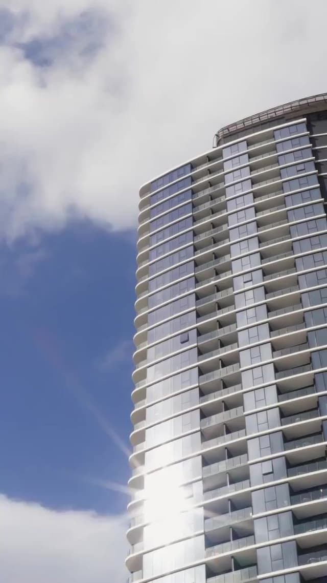A low angle view of a curved glass high-rise tower against a blue sky with clouds.
