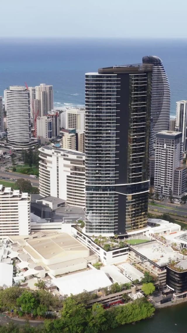 An aerial view of Gold Coast high-rises along the coastline, including a curved beachfront tower.