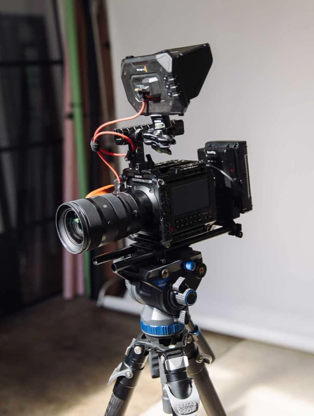 A professional cinema camera on a tripod stands ready in a studio, fitted with a monitor and prime lens.