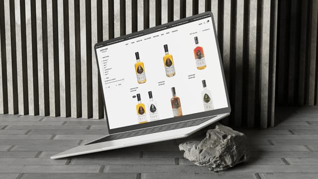 A laptop screen shows the Capricorn Distilling Co online shop with a grid of spirit bottles for sale.