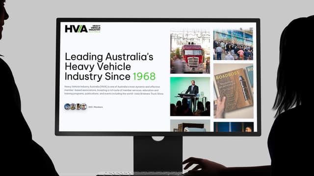 A monitor displays the Heavy Vehicle Industry Australia website homepage with truck photography and event imagery.