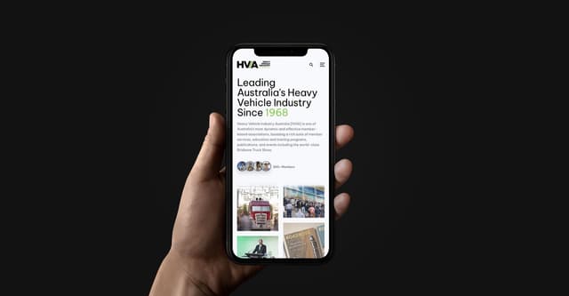 A hand holds a phone displaying the Heavy Vehicle Industry Australia website homepage against a dark background.