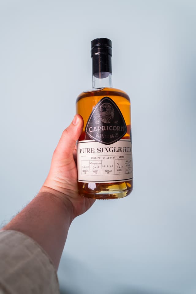 A bottle of Capricorn Pure Single Rum held against a pale blue wall