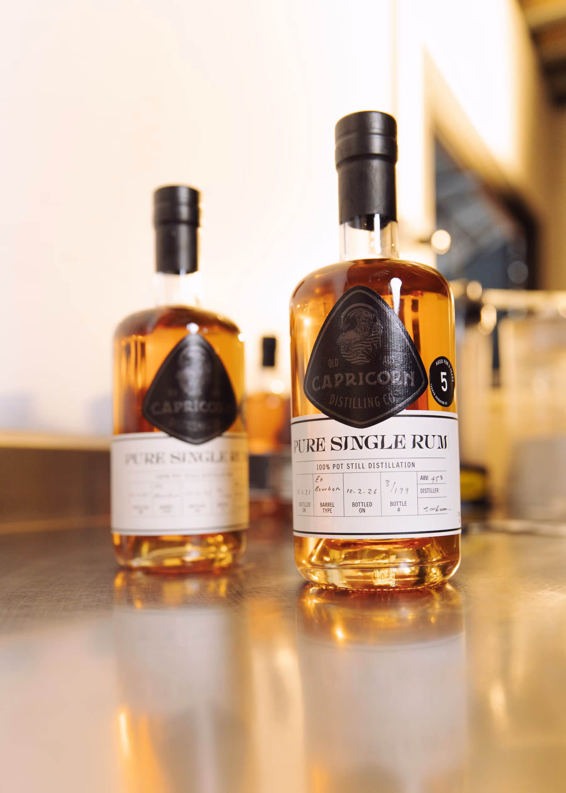 Two bottles of Capricorn Distilling Co Pure Single Rum standing on a bright bar top.