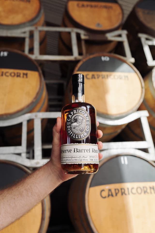 A bottle of Capricorn Reserve Barrel Rum held in front of the barrel racks
