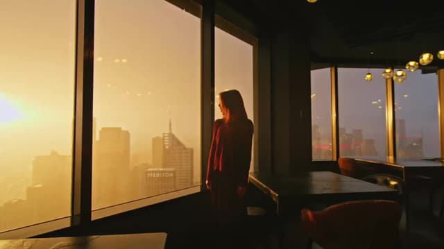 A woman stands at a floor to ceiling window overlooking a city skyline at dusk, a Fraser & Partners project.