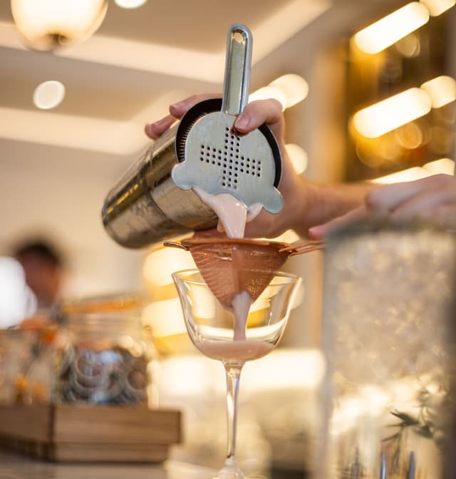 A bartender strains a pink cocktail through a Hawthorne strainer into a coupe glass at Hilton Surfers Paradise.