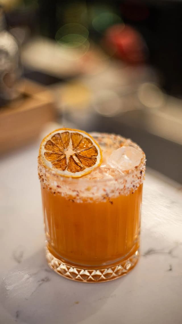 An orange cocktail garnished with a dried citrus wheel and a spiced salt rim on a marble bar at Hilton Surfers Paradise.