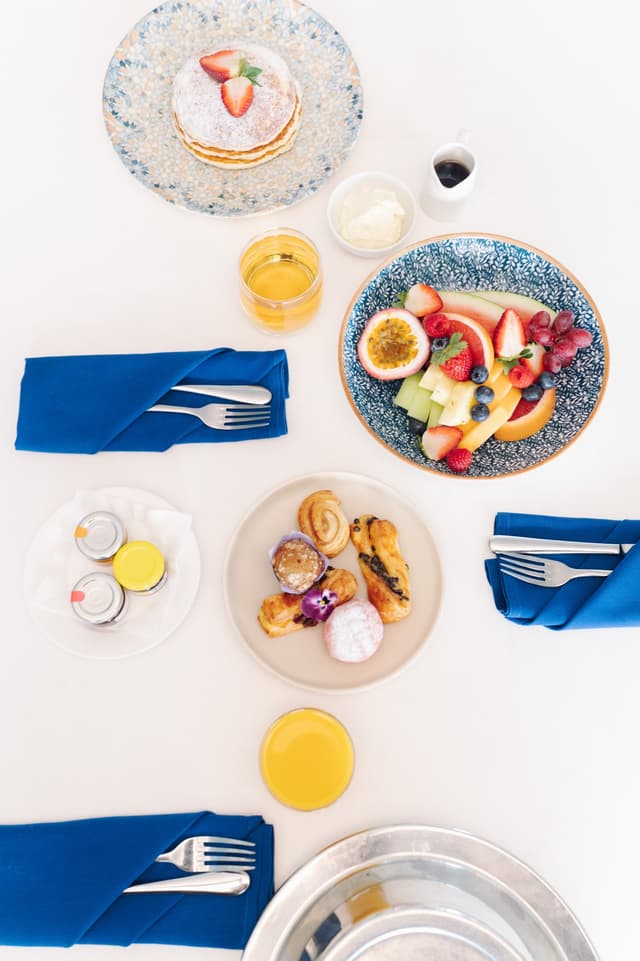 A Hilton Surfers Paradise breakfast spread includes pancakes, fresh fruit, pastries, and orange juice on blue linen napkins.