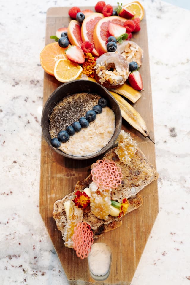 A breakfast board loaded with fresh fruit, glazed donuts, an oat bowl, and toast with honeycomb, styled for Hilton Surfers Paradise.