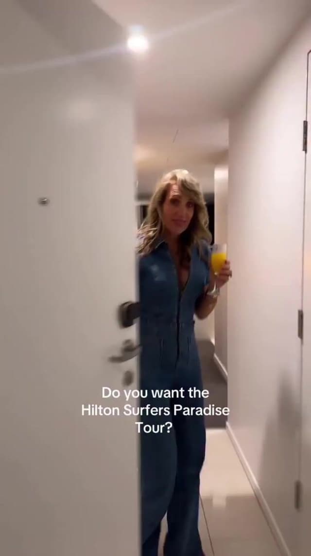 A woman holding a mimosa opens a hotel room door beside the text 'Do you want the Hilton Surfers Paradise Tour?'