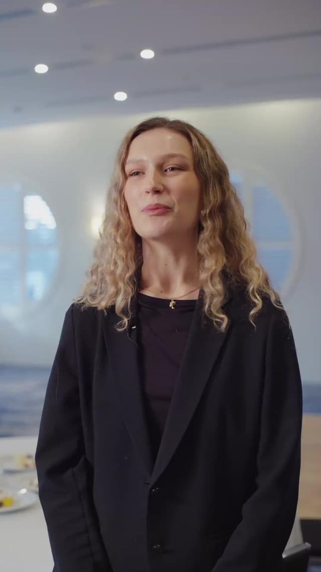 A woman in a dark blazer stands in a softly lit lobby for a Hilton Surfers Paradise video.