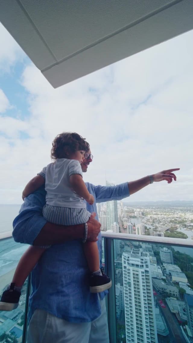 A father holds a child on his shoulders on a high rise balcony overlooking the Gold Coast skyline at Hilton Surfers Paradise.