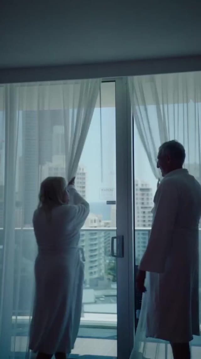 A couple in white robes look out from a high rise balcony over the Gold Coast skyline at Hilton Surfers Paradise.