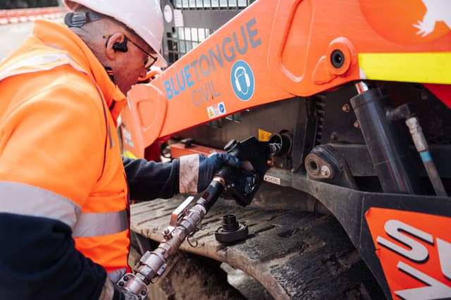 An operator coupling a diesel line to an excavator during an onsite refuel.