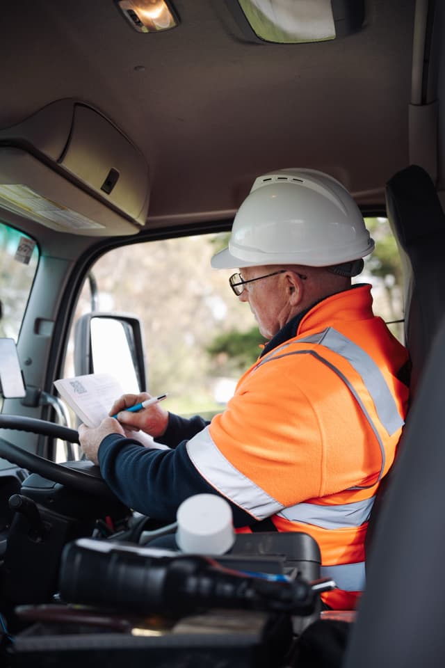 A Padthaway Resources driver in a hard hat and high vis jacket writes in a logbook inside a truck cab.