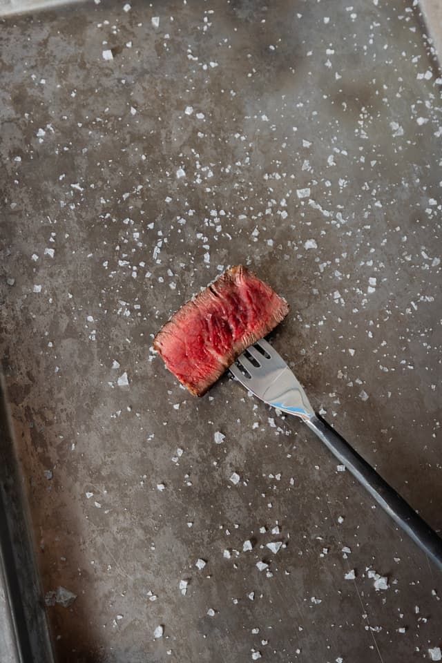 During a Providore Global shoot, a medium-rare steak slice rests on a fork over a salt-flecked steel tray.