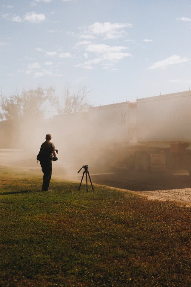 A videographer with a camera and tripod films a dusty truck departing a Providore Global farm.
